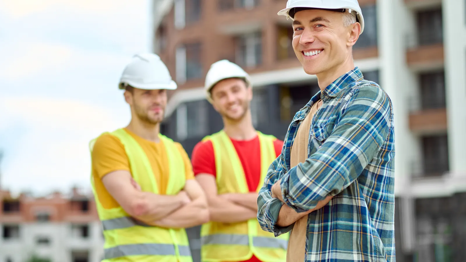Smiling safety-trained worker in a hard hat with two colleagues in hi-vis vests